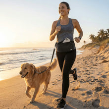 A woman jogs with her golden retriever at sunrise on an Australian beach, wearing athletic clothes and the Pawbella Dog Walking Bum Bag. Waves and palm trees dot the scenic background as she smiles, leash in hand.